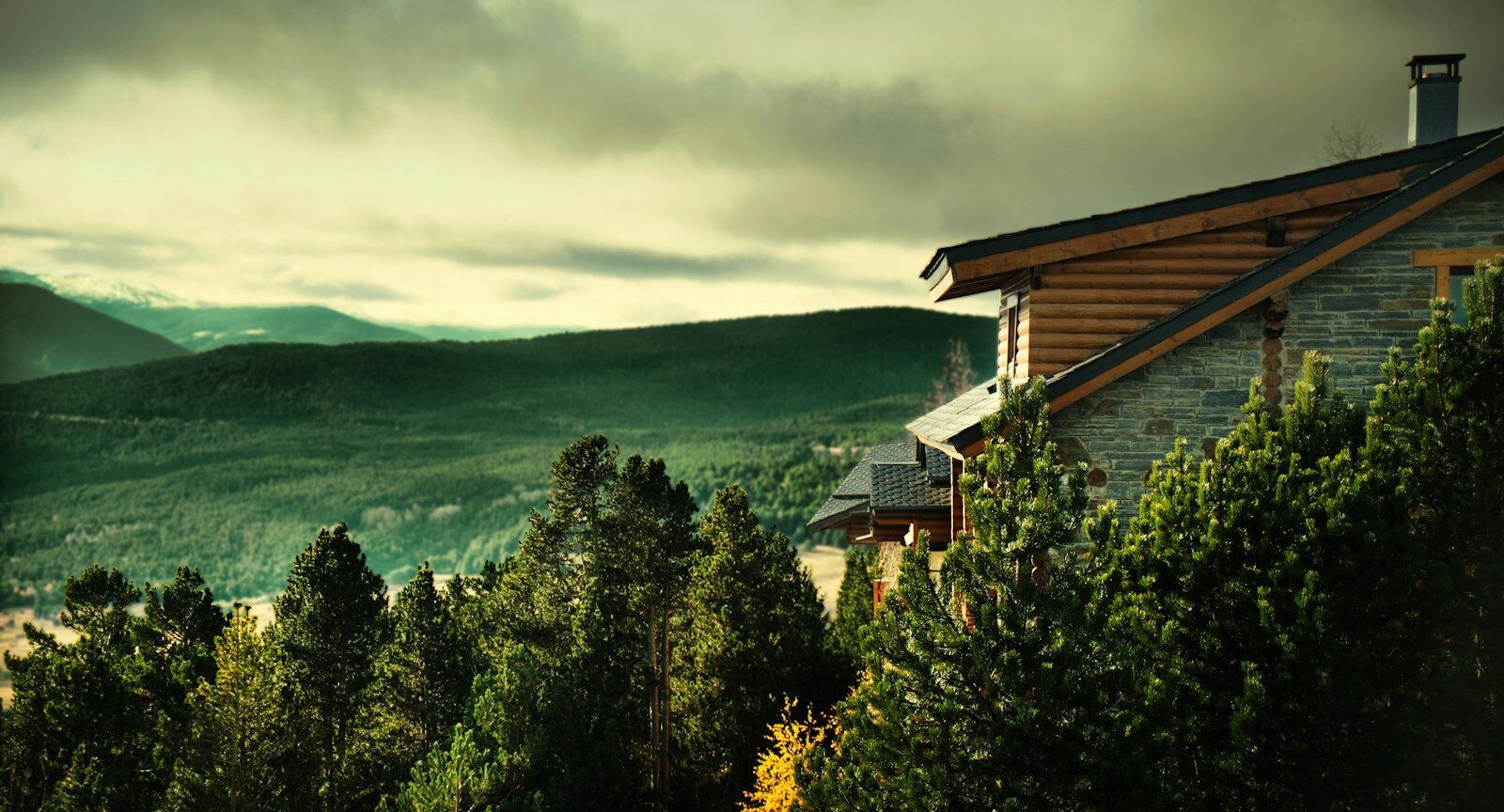 A stone and log cabin nestled among pine trees overlooking a mountain valley